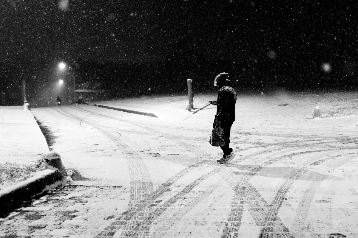 Une silhouette seule traverse une chaussée enneigée de Meudon, la nuit, sous les lumières des réverbères.