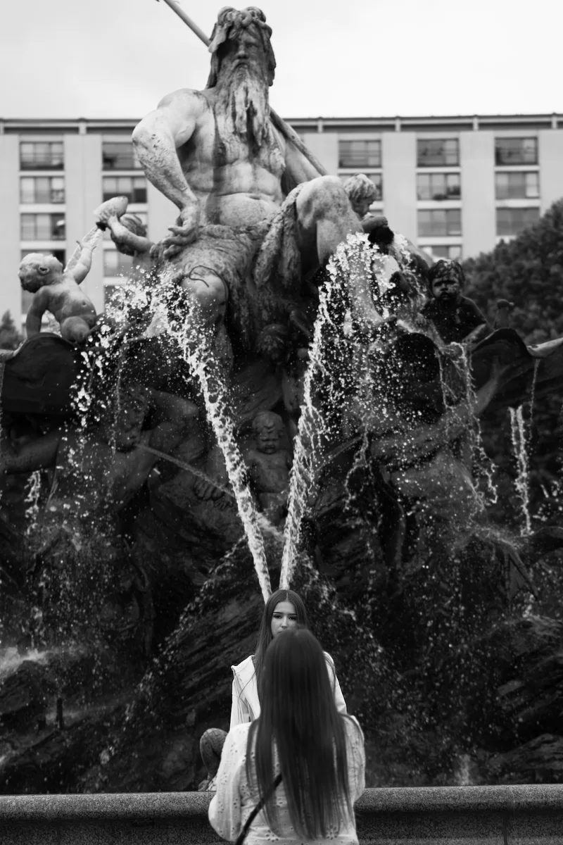 A young woman in front of the Neptune Fountain in Berlin. Two jets of water behind her head suggest wings.